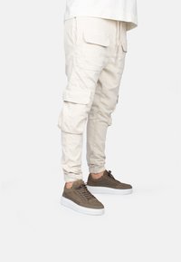 Pantalones cargo beige con bolsillos frontales y puños en los tobillos, combinados con zapatillas de ante marrón que cuentan con una suela blanca y diseño de cordones.