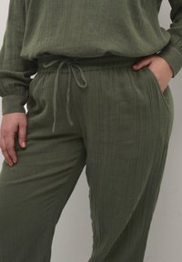 Olivenfarbene Loungewear-Set aus einem strukturierten Stoff mit vertikalen Streifen, elastischen Taillenbund und seitlichen Taschen an der Hose.