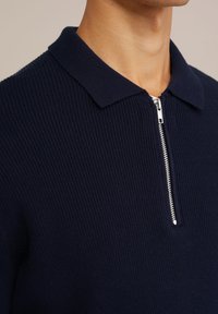Marinblå ribbad pikétröja med fackfäste framtill, med klassisk krage och texturerad tyg.