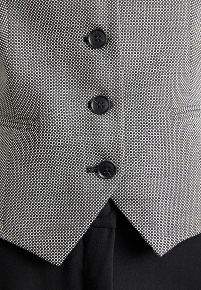 Melnbalts ar punktiņiem, pieguļošs vestes modelis, ar piecām melnām pogām un V formas apakšmalu. Izgatavots no teksturēta auduma.