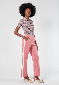 Kurzärmliges, kragenshirt mit einem geometrischen Muster in Pink und Schwarz. Pinke Hosen mit weißen Seitenstreifen, tailliertem Bund und Taschen.