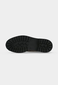 Semelle en caoutchouc noir d'une chaussure avec des rainures profondes et des motifs en forme de croix pour l'adhérence sur un fond clair uni.