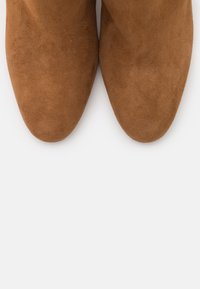 Brune ruskinds-ankelstøvler med smal, spids tå og tekstureret overflade. Ingen synligt hardware eller karakteristiske mønstre. Ensfarvet design.