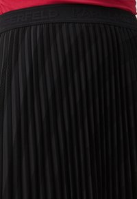 Black pleated skirt featuring a textured design with cutout patterns. Waistband displays embossed "KARL LAGERFELD" branding.