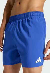 Modré športové šortky vyrobené z ľahkého materiálu majú elastický pás a biele logo na dolnom leme.