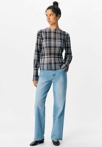 Svart och vit rutig långärmad topp i kombination med ljusblå rakbenjeans och svarta slip-on skor; mjukt tyg med en avslappnad passform.