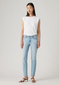 Világoskék farmer skinny nadrág, közepes derékkal, egy testhez simuló, ujjatlan fehér topot viselve. A fekete pántos magassarkú cipő teszi teljessé a megjelenést.