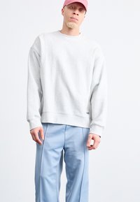 Sweatshirt gris clair à coupe décontractée et poignets côtelés, associé à un jogging bleu clair avec des coutures latérales. Design simple, sans motifs.