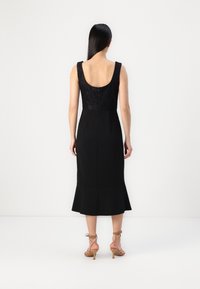 Melnā kleita ar pieguļošu augšdaļu un mežģīņu detaļām, ar izplestu apakšdaļu un aizmugurēju rāvējslēdzēju. Modelis valkā brūnas siksniņu kurpes.