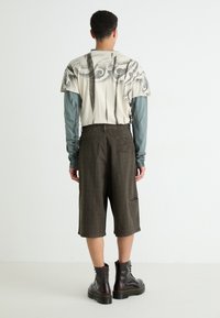 T-shirt graphique surdimensionné en crème avec des motifs noirs, associé à un short marron jusqu'aux genoux avec une poche et des rayures discrètes. Bottes marron.