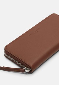 Brown leather wallet with a smooth texture, featuring a silver zipper and a wrist strap. Engraved logo detail on the front.