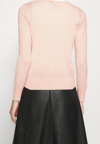 Suéter de color rosa claro con mangas largas y escote redondeado, combinado con una falda de cuero negra con detalles de costura.