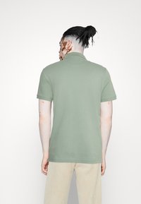 Světlá zelená polo tričko s krátkými rukávy a límcem, vyrobené z měkké tkaniny. Má jednoduchý design a rovný lem, z pohledu ze zad.