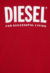 T-shirt in cotone rosso con bold text bianco "DIESEL" e un testo più piccolo "FOR SUCCESSFUL LIVING" sotto. Texture liscia, design con colletto a girocollo.