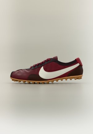 Niska sportowa but w bordowym i brązowym kolorze z białym logo Nike i teksturowaną gumową podeszwą, pokazana z boku na neutralnym tle.