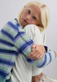 Suéter de punto a rayas en tonos verde, azul y lavanda; textura suave; combinado con pantalones crema y zapatos grises. La tela tiene un aspecto esponjoso.