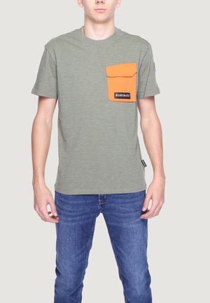 T-shirt verde oliva con finitura testurizzata, caratterizzato da una tasca sul petto arancione a contrasto e un marchio, abbinato a jeans blu.