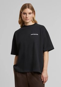 Zwart oversized t-shirt van katoen, met korte mouwen en de tekst "PROHIBITED" in het wit aan de linkerkant. Eenvoudig, minimalistisch ontwerp.