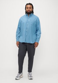 Jasnoniebieska koszula na guziki z długimi rękawami i kieszenią na piersi, zestawiona z ciemnoszarymi spodniami oraz szarymi tenisówkami z białymi akcentami.