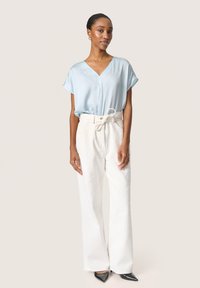 Maglietta azzurra chiara a maniche corte con scollatura a V, abbinata a pantaloni a gamba larga crema con texture e tacchi neri a punta.