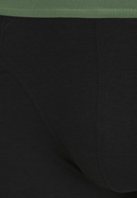 Schwarze Baumwollunterwäsche zeichnet sich durch eine glatte Textur mit einem kontrastierenden grünen Bund aus. Das Design umfasst eine schlichte, figurbetonte Form mit Nähdetails.