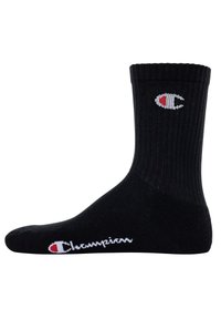 Schwarze Crew-Socke mit gerippter Textur, die ein kleines weißes und rotes Logo an der Seite und den Text "Champion" nahe der Zehe aufweist.