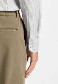 Camicia da uomo a righe grigio chiaro con polsini abbottonati, abbinata a pantaloni in velluto a coste marrone chiaro con una tasca e un dettaglio logo sottile.