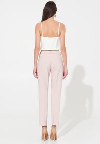 Weißes Croptop mit dünnen Trägern, kombiniert mit hellrosa, taillierten Hosen. Glatte Textur, figurbetontes Design und spitze, nudenfarbene High Heels.