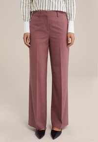 Vidbenade byxor i ett ljust mauve-tyg, med en slät textur, framfickor, en skräddarsydd midja och svarta spetsiga klackar.