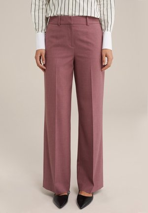 Vidbenade byxor i ett ljust mauve-tyg, med en slät textur, framfickor, en skräddarsydd midja och svarta spetsiga klackar.