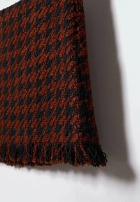 Coperta intrecciata in tonalità di nero e arancione bruciato, caratterizzata da un motivo a quadri houndstooth testurizzato e bordi frangiati.