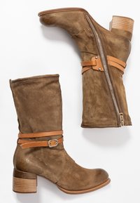 Brown suede ankle boots with a rounded toe, a block heel, and a side zipper. Features a tan leather strap with a buckle detail.