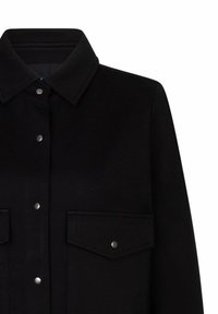 Zwarte button-up jas met puntige kraag en twee voorkantflapzakken die zijn beveiligd met drukknoopjes op een witte achtergrond.