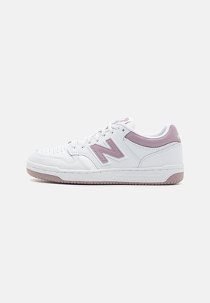 Hvide og lilla New Balance lavt snørestøvle med snørelukning foran og perforeret tå på en ensfarvet hvid baggrund.