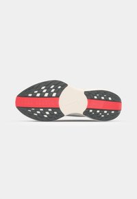 Semelle de chaussure Nike avec un fond en caoutchouc noir texturé, une bande d'accent rouge et des détails blancs, conçue pour la traction et le soutien.