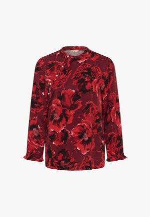 Piros, hosszú ujjú blúz nagy fekete és piros virágmintával, gyöngygombos részletekkel és fodros díszítéssel az elején és az ujjak végén.