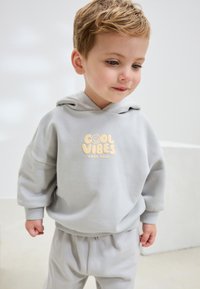 Helehall hall kapuutsiga dressipluus ja dressipüksid, millel on tekst "COOL VIBES" ja naerunäo graafika. Pehme materjal, lõdvestunud lõige, soonilised detailid.