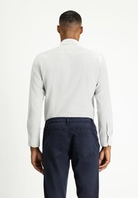 Camisa blanca de manga larga con tejido texturizado, cuello puntiagudo y puños abotonados, combinada con pantalones elásticos azul marino de cintura alta con bolsillos traseros.