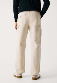 Beige Baumwoll-Cargohosen in lockerer Passform, mit zwei Gesäßtaschen und einer Seitentasche, auf einem neutralen Hintergrund.