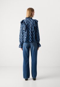 Blusa blu con motivo a fantasia e spalle arricciate, caratterizzata da una stampa a cuori. Abbinata a jeans blu a vestibilità comoda e scarpe nere.
