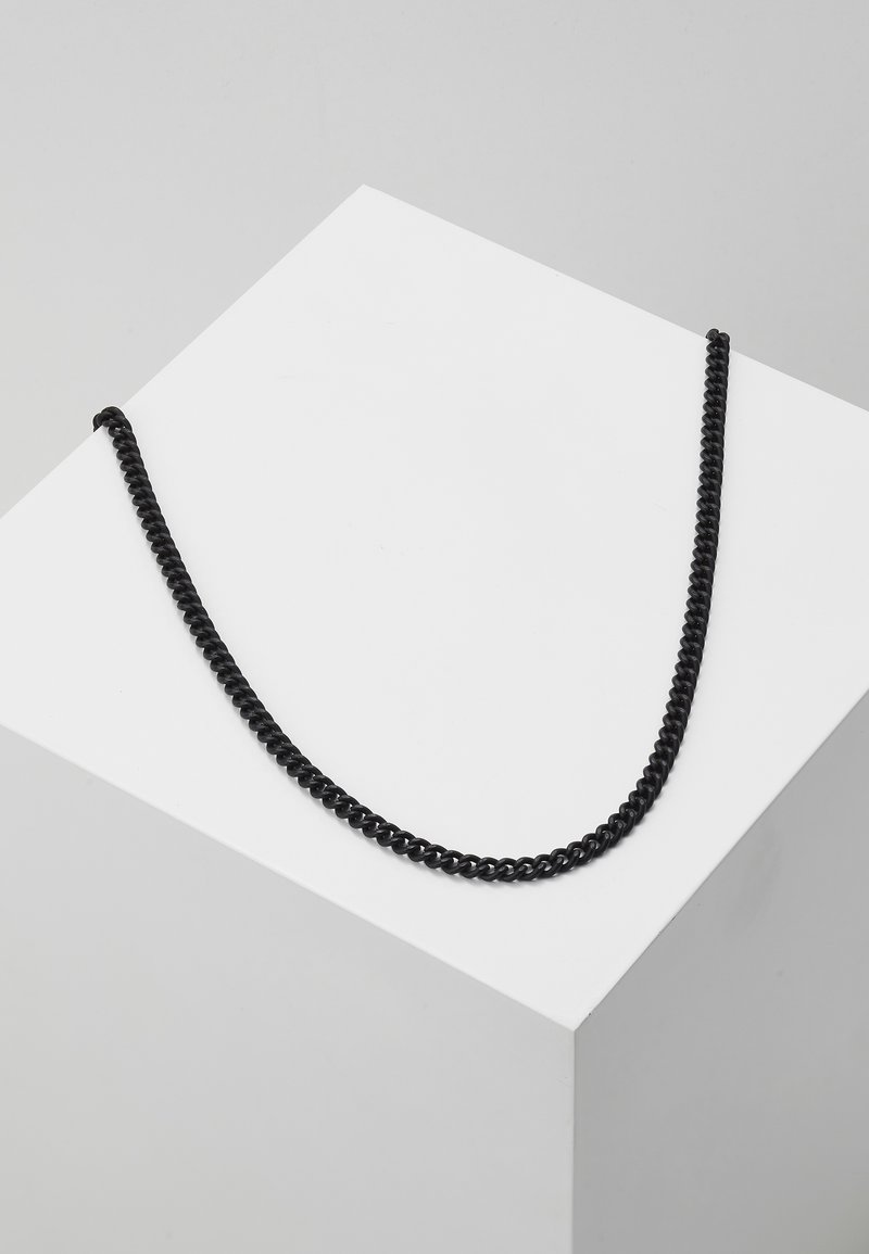 Chaîne noire avec des maillons torsadés, conçue pour pendre en forme de U, présentée sur un piédestal géométrique blanc.