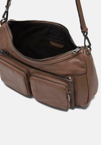 Bolso de hombro de cuero marrón con cierre de cremallera, que cuenta con dos bolsillos frontales con cremallera y una textura suave, además de un interior forrado en tela negra.