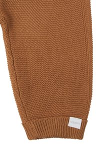 Pull en tricot marron avec un motif texturé, des manches bord-côtes et une petite étiquette sur le côté inférieur gauche.