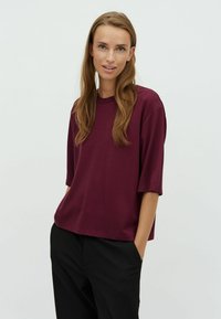 Burgundy short-sleeve t-shirt made of soft fabric with a relaxed fit and crew neckline. Paired with black trousers featuring side pockets.