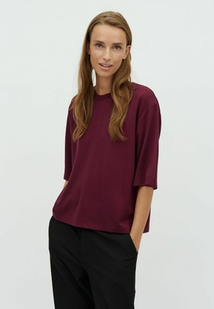 Burgundy short-sleeve t-shirt made of soft fabric with a relaxed fit and crew neckline. Paired with black trousers featuring side pockets.