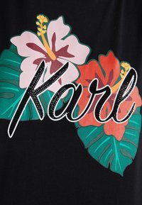 Tela negra con flores rosas y rojas y hojas verdes. El nombre "Karl" está adornado con letras negras brillantes.