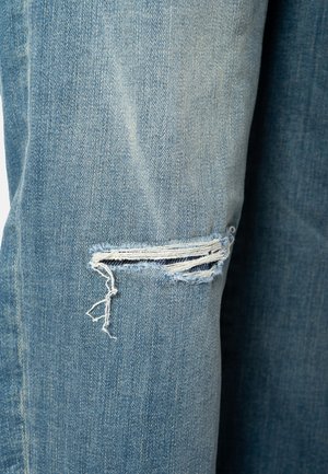 Tissu en denim bleu clair avec une déchirure horizontale et des bords effilochés sur un jean.