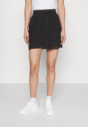 Nainen, joka pukeutunut mustaan kulutettuun denimminihameeseen, jossa on korkea vyötärö, yhdistettynä valkoisiin sukkiin ja valkoisiin korokepohjakenkiin.