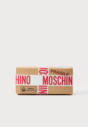 Brauner Karton, umwickelt mit rot-weißem Klebeband mit der Aufschrift "MOSCHINO" und "ZERBRECHLICH", mit einem "HANDLE WITH STYLE"-Symbol an der Seite.