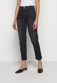 Jeans in denim scuro con una vestibilità classica, dotati di cinque tasche, una tasca anteriore piccola e un lavaggio sottile. Abbinati a mule nere su uno sfondo neutro.